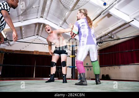 Wrestler screaming in pain while rival fighting during match Stock Photo