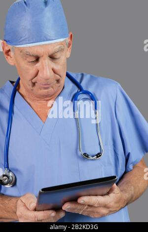 Senior male surgeon using tablet PC over gray background Stock Photo