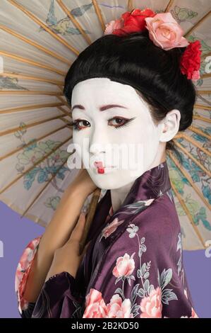 Close-up of Japanese woman with painted face holding parasol against purple background Stock Photo