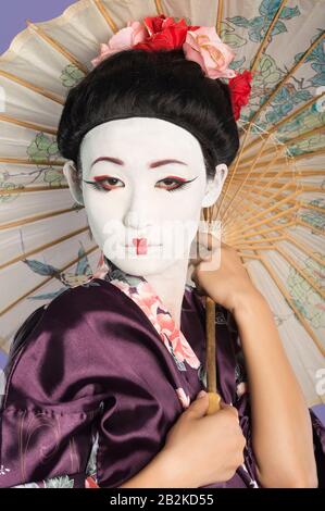 Close-up of Japanese woman with painted face holding parasol against purple background Stock Photo