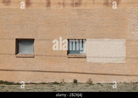 a pair of square vintage windows on the facade of a brown brick wall warehouse building Stock Photo