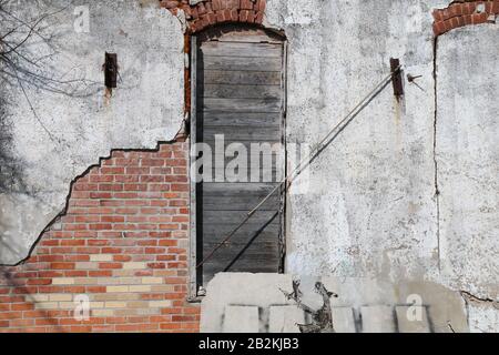 a boarded up arched window on a faded stucco red brick wall building Stock Photo