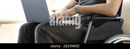 Man sitting in wheelchair working with laptop computer Stock Photo