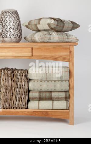 Sideboard style wooden beach table with natural coloured cushions, throws and ornaments and wicker baskets on a white background Stock Photo