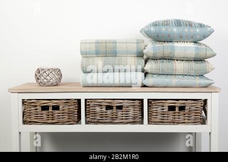 Sideboard style white wooden table with blue coloured cushions, throws and ornaments and wicker baskets on a white background Stock Photo