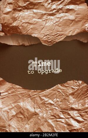The words Time To Upgrate.appearing behind torn bronze foil. Business concept for updating something Stock Photo