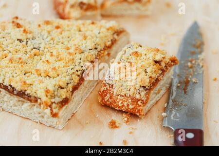 Sweet sand tart with apricot jam. Cut into pieces, lying on a board with a kettle in the background. Teapot with cups of tea with a sweet cake Stock Photo