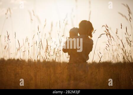 Happy child and his mom have fun outdoors in a field flooded with . Mom holds the child in her arms, and the child hugs and kisses the mother Stock Photo