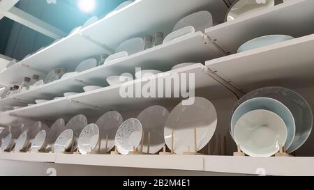 Many white plates stand on white shelves of display cases. Horizontal. Wide Stock Photo