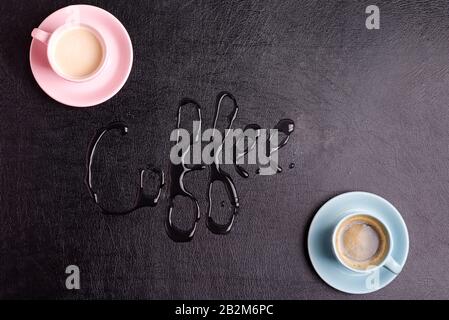 Creative backdrop with two ceramic cups of freshly brewed aromatic morning drink and text written from water drops on a decorative black artificial ec Stock Photo