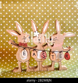 Three wooden Easter bunnies with painted decoration and the text Easter written on eggs. Stock Photo