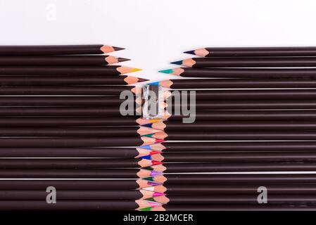 Creative pattern from multicolored pencils and sharpener in the shape of fastened zipper on a white background with copy space. Top view. Stock Photo