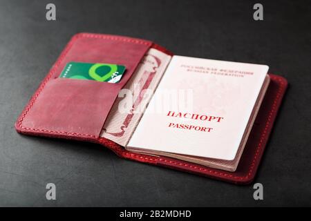 Red handmade passport cover made of genuine leather on a dark background, revealed with a passport and a green electronic card. Passport of a citizen Stock Photo