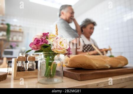 Selective focused on rose on table in kitchen with elder senior asian couple cooking dinner  in background.love is all around and everywhere. Stock Photo