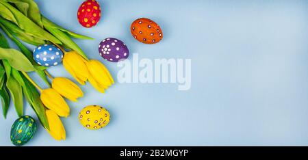 Easter eggs. Happy easter card. Easter eggs on a blue background. Eggs laid out in a row. Happy easter. Tulips. Yellow tulips and colored eggs are sca Stock Photo