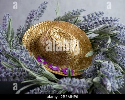 Straw cowgirl or cowboy hat decorated with purple felt flowers on top of a lavender flower wreath with a black and plaster background.  Simple country Stock Photo
