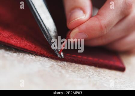 A leather craftsman works with leather. Sews leather goods. Making things handmade. Women's hands with a needle, thread, scissors and a blowtorch. Clo Stock Photo