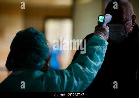 Otopeni, Romania - February 25, 2020: A woman in a protective suit measures the temperature of a man inside the Henri Coanda International airport for Stock Photo