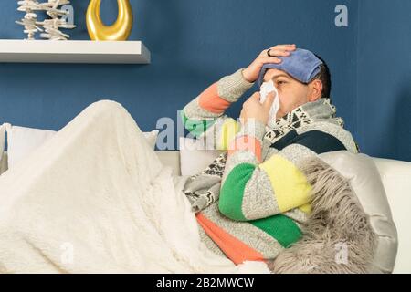 A sick man with a rag on his head and a handkerchief in his hand is lying on his couch Stock Photo