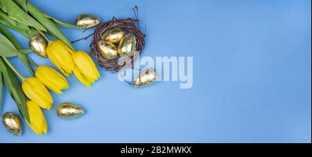 Easter eggs. Happy easter card. Easter eggs on a blue background. Happy easter. Tulips. Yellow tulips and near golden eggs in the nest. View from abov Stock Photo