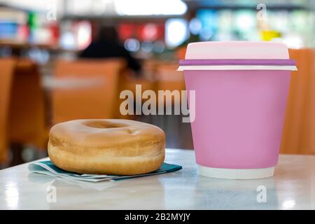 A pink disposable cup with coffee and a donut on a coffee shop table Stock Photo