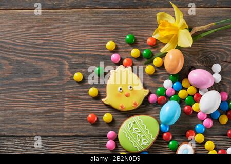 Crop of colorful ginger glazed cookies and chocolate balls and daffodil isolated on wooden background. Close up of homemade lovely delicious pastry in Stock Photo