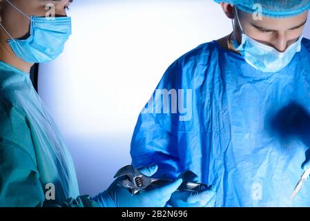 close-up, portrait of two surgeons, in medical masks and a sterile gown. the assistant passes the wrench to the surgeon. Medical humor. Surgical joke. Stock Photo