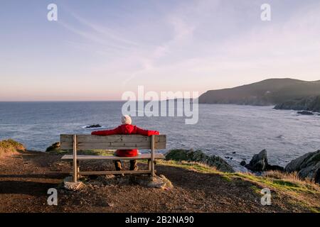 Man relaxing on a woden bench in Loiba Cliffs, Ortigueira, Spain Stock Photo