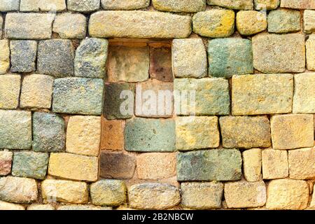 A close-up view of a weathered stone wall constructed from irregularly shaped, rough-hewn stones in varying shades of beige, gray, green, and yellow. The stones are arranged in horizontal courses Stock Photo
