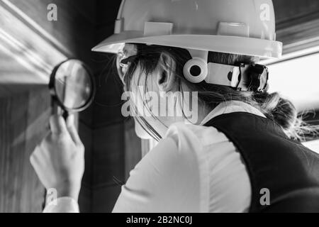 close up on woman inspector using a magnifying glass during air inspection, looking for molds or fungi on the wooden window edge. black and white. Stock Photo