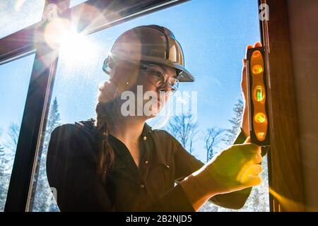 close up on worker woman uses spirit level on vertical surface next to a window with sun in the sky view. construction inspector, architect concepts Stock Photo