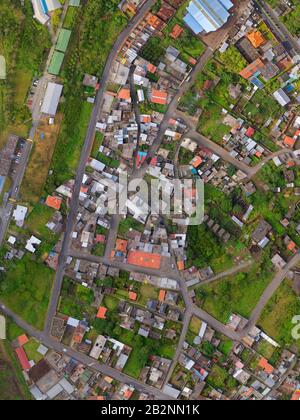 An overhead aerial photograph captures a densely packed residential area with narrow winding roads and closely spaced houses featuring varied roof colors including red, gray, and blue. The Stock Photo