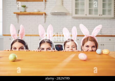 Happy easter. Mother and daughters with rabbit ears decorate Easter eggs at a table in kitchen. Stock Photo