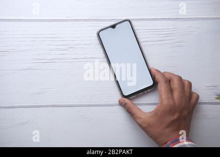 Man holding smartphone with empty screen on wooden table  Stock Photo