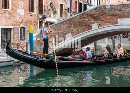 Gondolier in traditional striped top busy on his mobile phone as he steers his gondola, venice, italy. Stock Photo