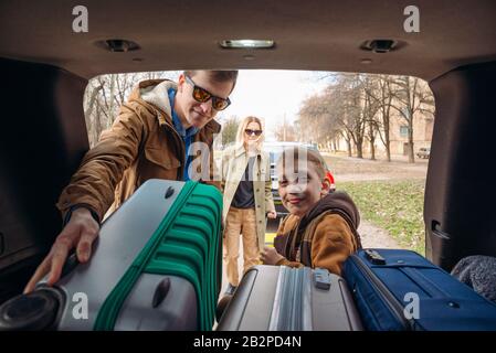 family with kid putting bag in car trunk Stock Photo
