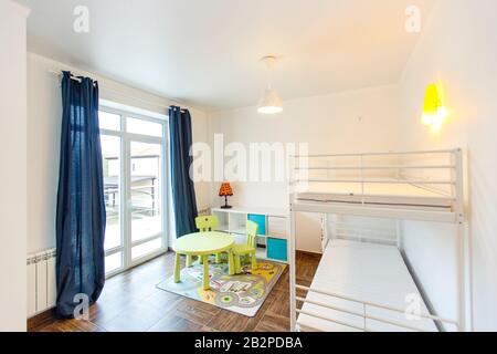 Children's room in the cottage. Bunk bed, window with blue curtains, large wardrobe with yellow doors. Stock Photo