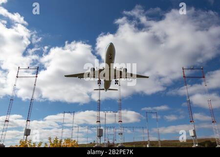 Large aircraft seen overhead landing over runway approach lights on a partly cloudy day. Stock Photo