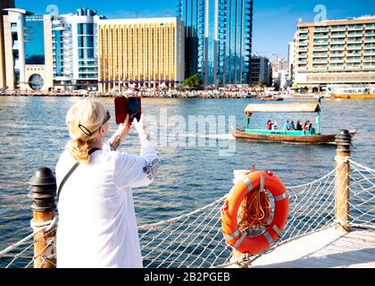 back view of Woman tourist taking photos with her mobile phone at Dubai Creek UAE Stock Photo