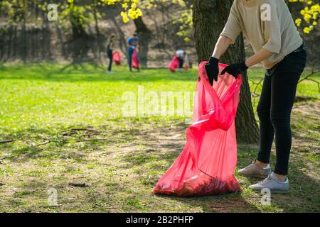 Man and woman volunteer wearing picking up trash and plastic waste in public park. Young people wearing gloves and putting litter into red plastic bag Stock Photo