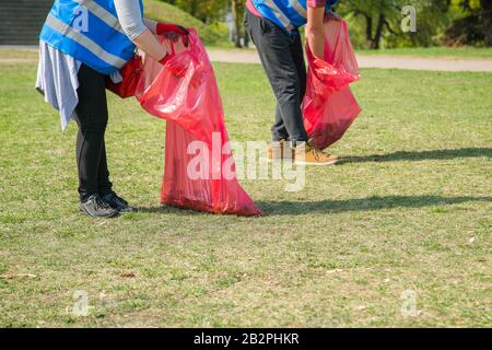 Man and woman volunteer wearing picking up trash and plastic waste in public park. Young people wearing gloves and putting litter into red plastic bag Stock Photo