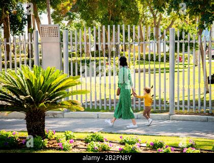 Mother and child walking hand in hand along palm lined walkway in colour Stock Photo