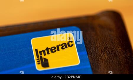 Interac, a Canadian interbank network logo on a blue card, atop of brown wallet. Stock Photo