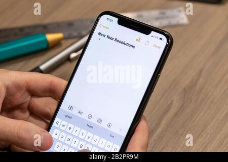 Man typing a note on a smartphone titled “New Year Resolutions” while sitting a desk. Stock Photo