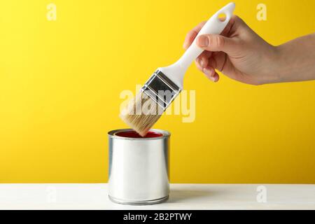 Female hand holding brush over the can with red paint against yellow background Stock Photo