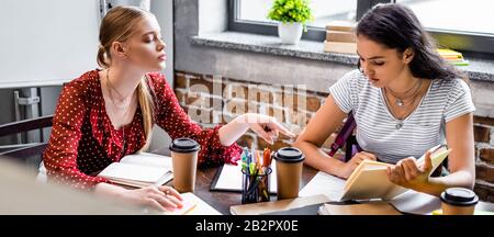 panoramic shot of attractive multicultural friends sitting at table and studying in apartment Stock Photo