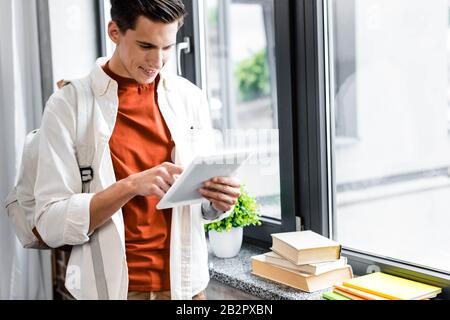 handsome student smiling and using digital tablet in apartment Stock Photo