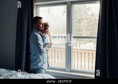 Middle age Caucasian father trying to calm down newborn baby. Man parent holding rocking child on his hands. Authentic lifestyle family moment. Single Stock Photo