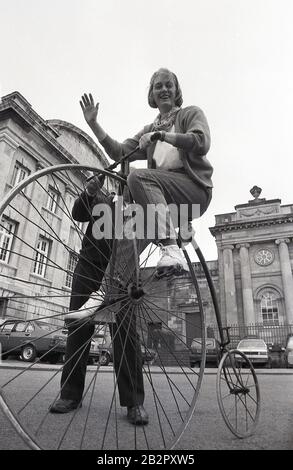 1980s, historical, a woman sitting on a penny-farthing bicycle, also known as a high wheeler or an ordinary. Popular in the 1870s and 80s, with its large front wheel and small back wheel, it was the first machine to be known as a 'bicycle'. Difficult to mount and to ride and with a danger of falling off, given the height of the front wheel, it was superceded by the modern 'safety bicycle'. Stock Photo