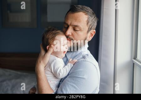 Middle age Caucasian father trying to calm down newborn baby. Man parent holding rocking child on his hands. Authentic lifestyle family moment. Single Stock Photo